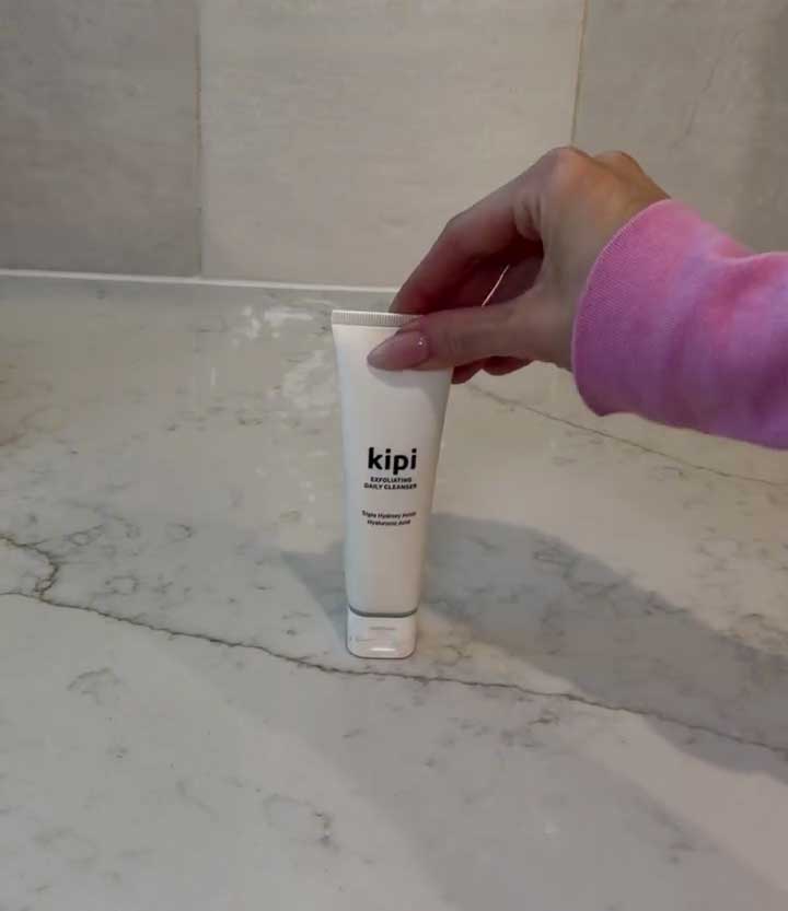 Hand holding a tube of 'kipi' cleanser on a marble surface