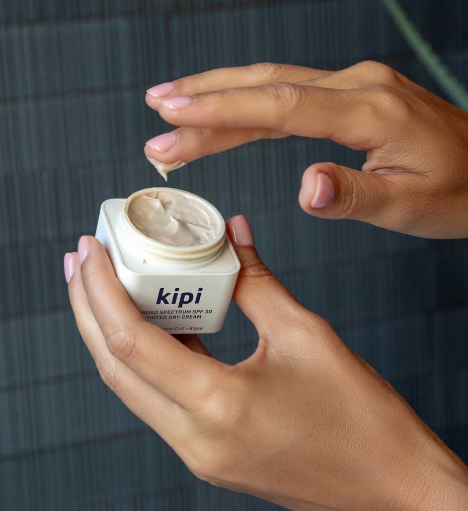 Person holding a jar of 'Kipi' cream against a blurred background