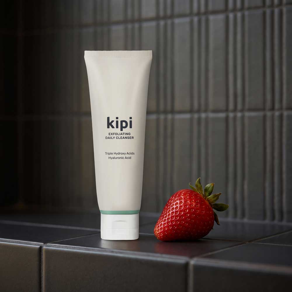 Kipi exfoliating daily cleanser tube with a strawberry on a tiled surface