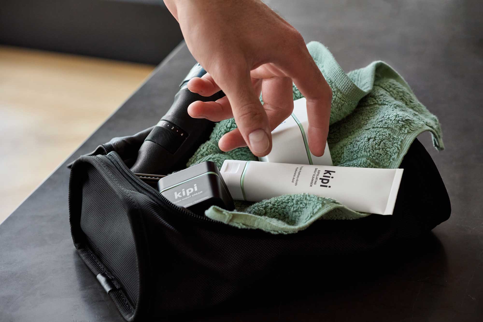 Hand reaching for a skincare product on a towel inside a black bag