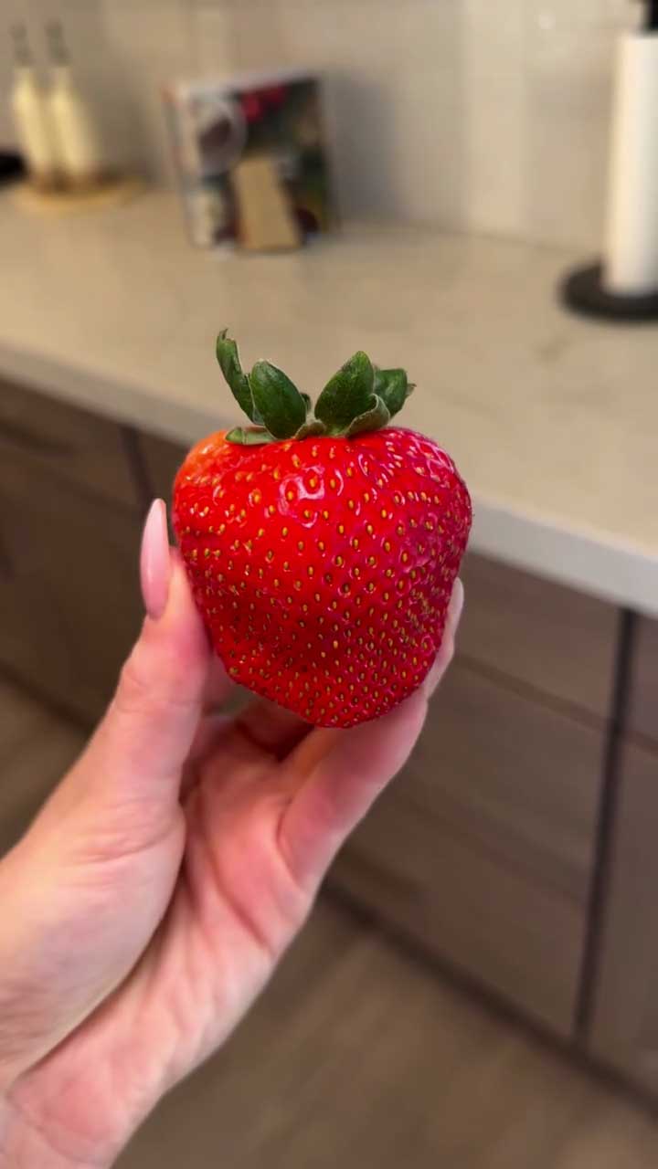 Hand holding a red strawberry in a kitchen setting