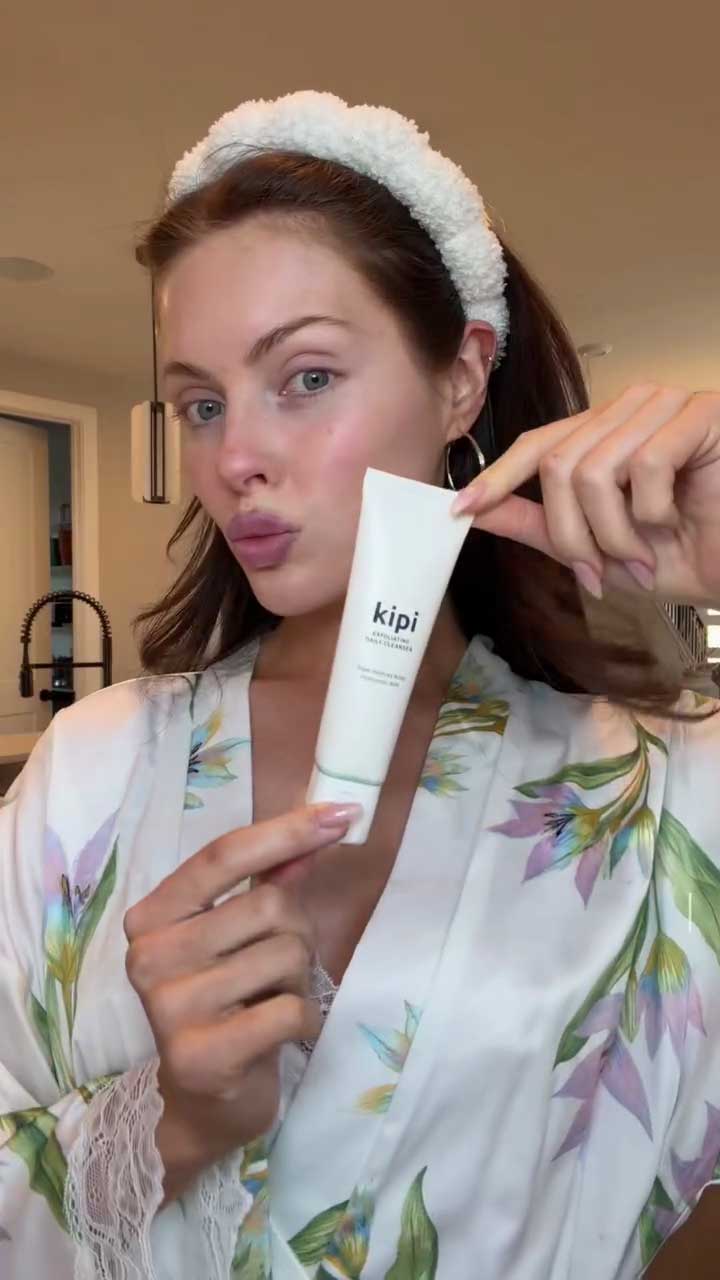Woman holding a 'kipi' skincare product in a home setting