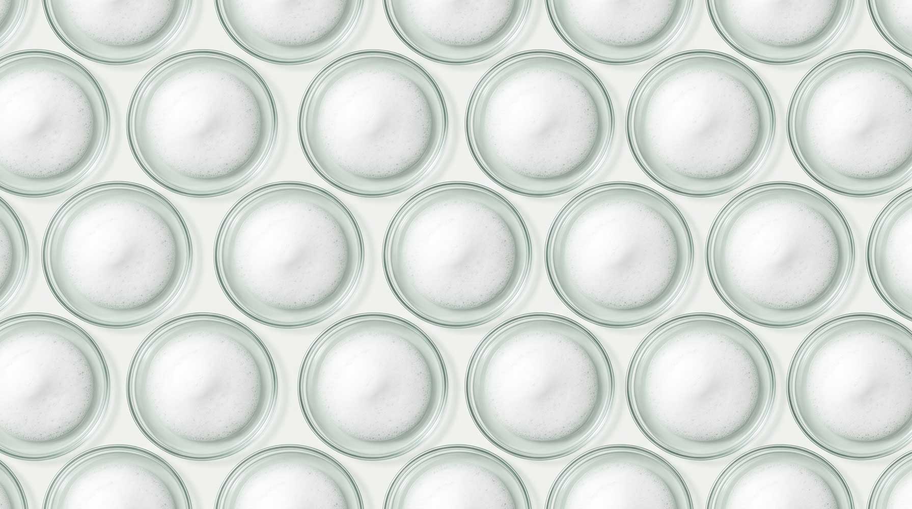 A patterned background of small glass dishes full of foam from lathered face cleanser.
