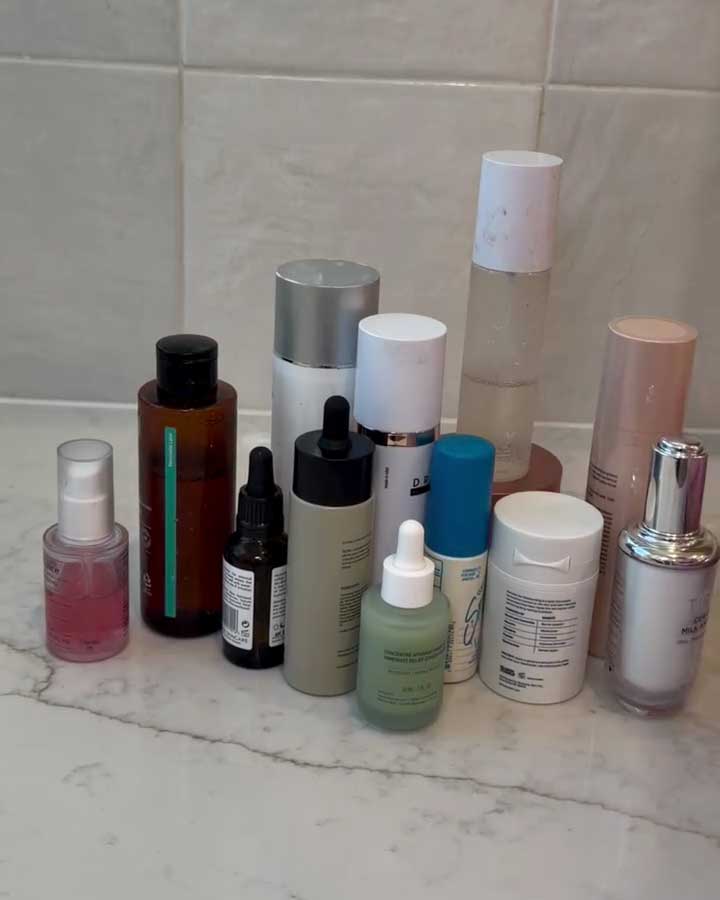 Collection of skincare and cosmetic bottles on a bathroom counter with tiled wall background