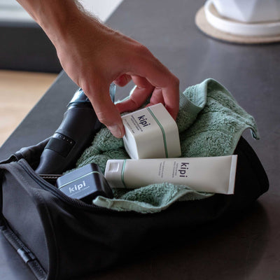 Person reaching for Kipi skincare products on a towel with a black bag in the background