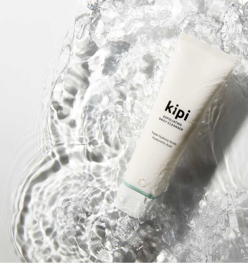 Kipi exfoliating daily cleanser bottle with water droplets on a light gray background