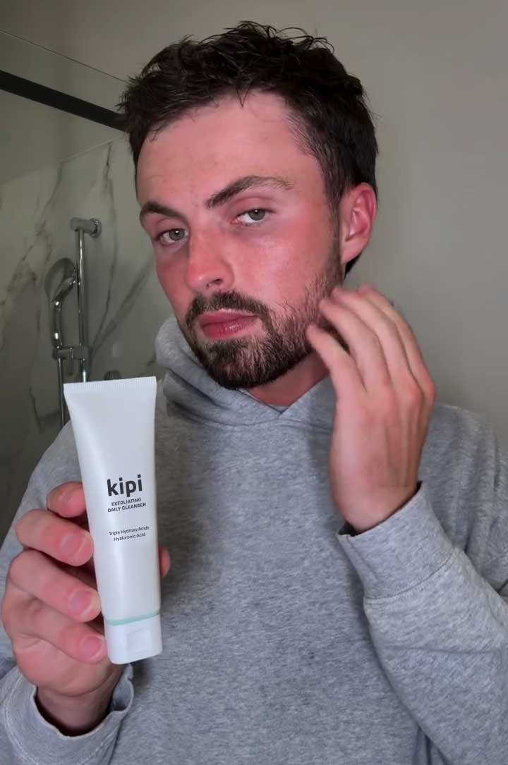Man holding a tube of Kipi skincare product in a bathroom setting
