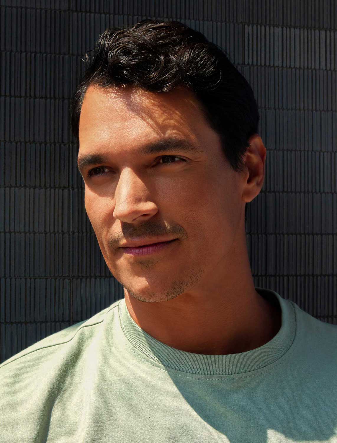 Man wearing a light green shirt against a dark textured wall