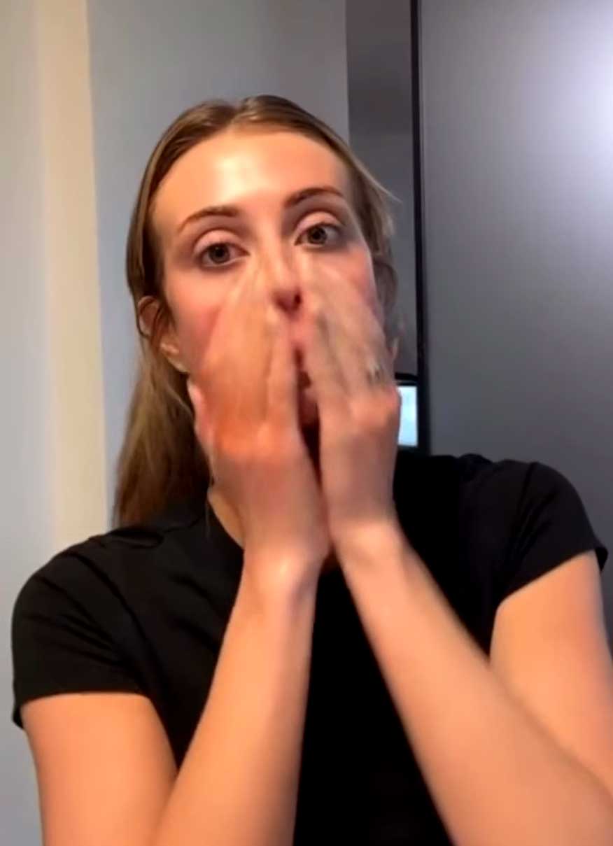 Woman scrubbing her face with skin cleanser while looking in the mirror.