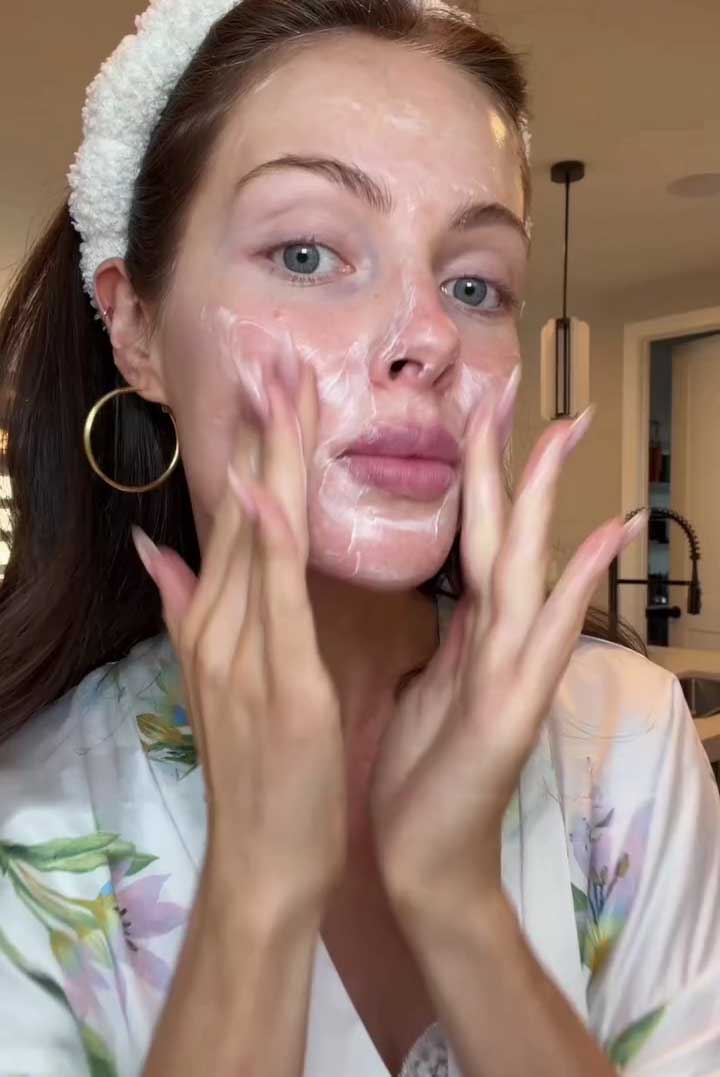 Woman applying a facial cleanser in a home setting